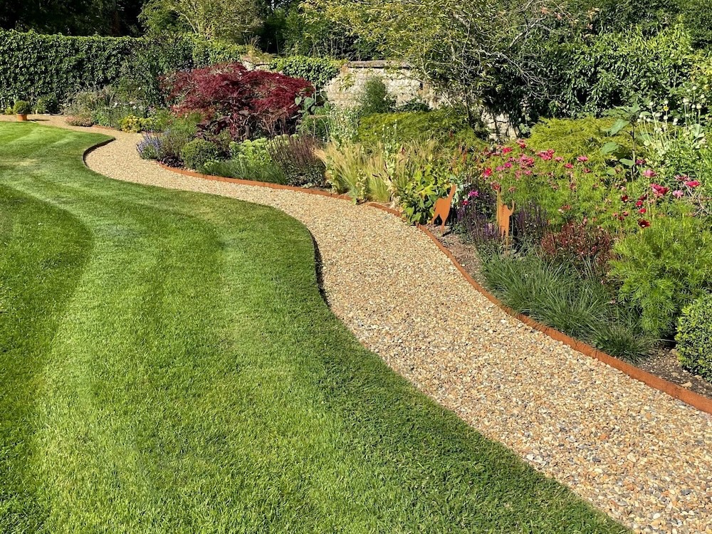 A freshly mown suburban front lawn and garden beds beside a home, in soft morning light